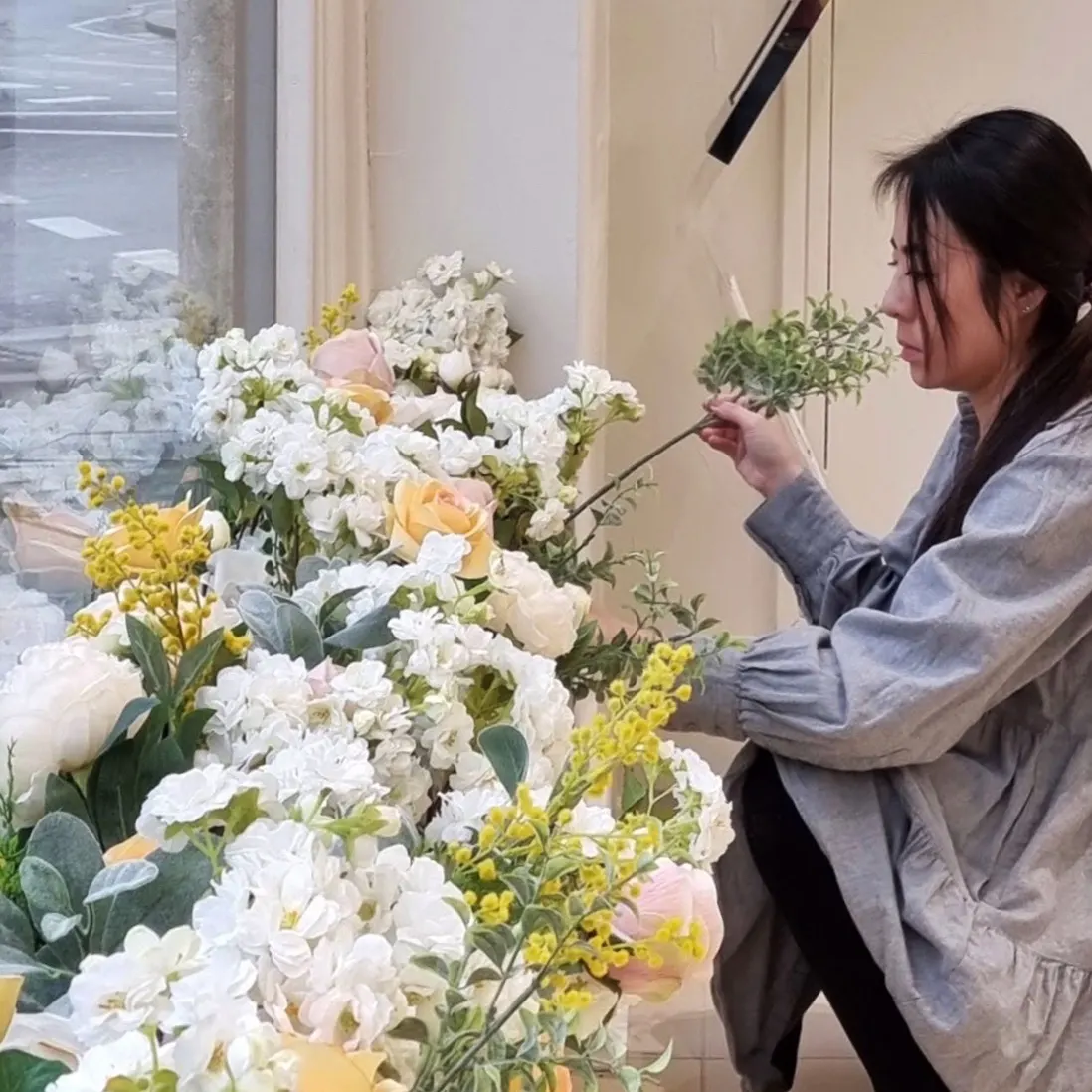 A florist placing a stem into a large cream and white floral installation in a showroom window