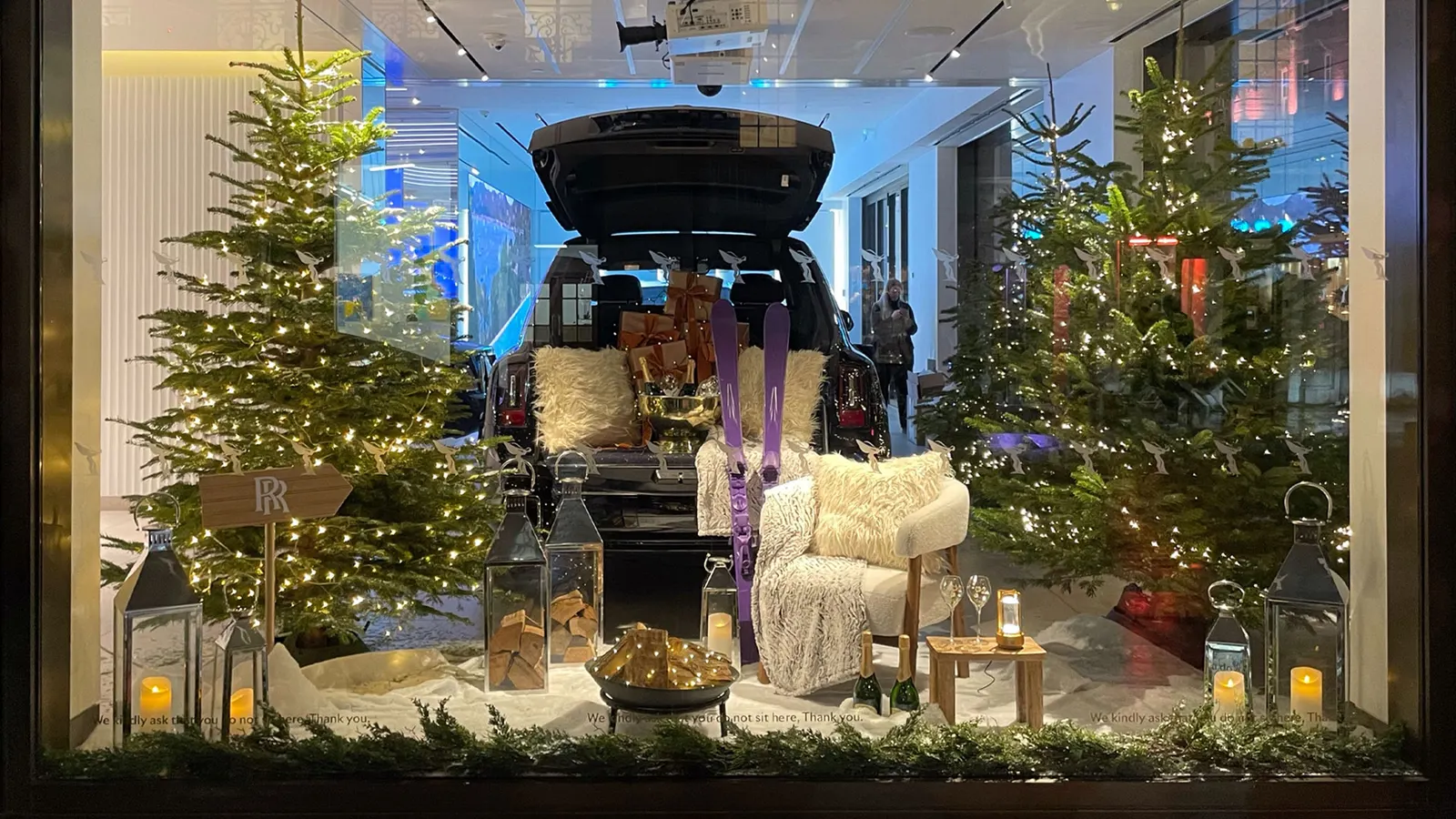 A winter window installation in a car showroom, with lit Christmas trees, lanterns and candles in artificial snow
