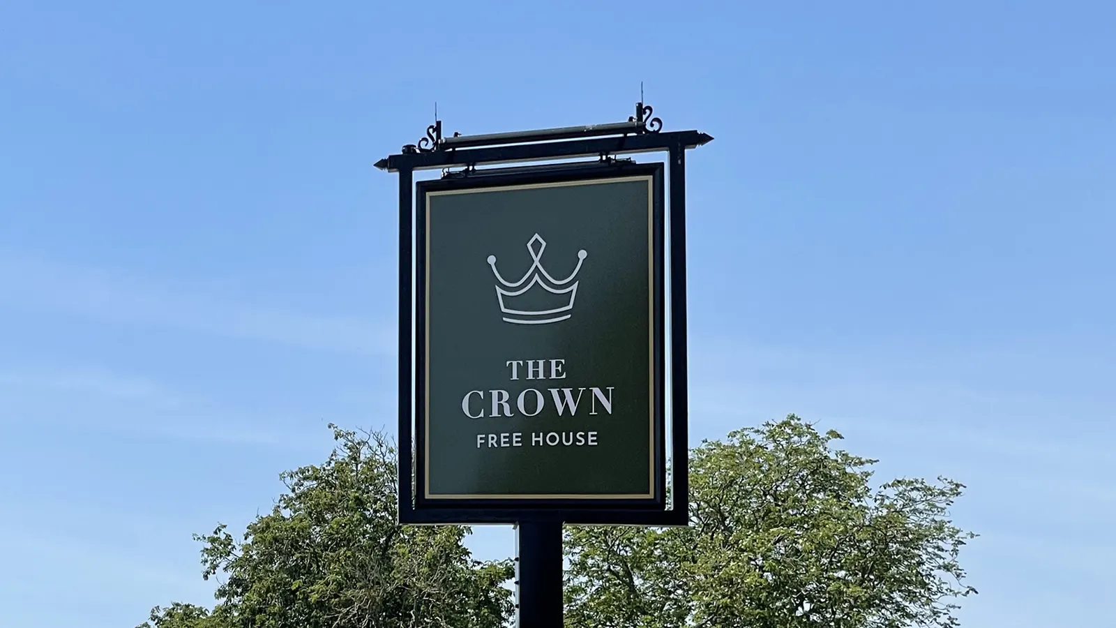 A hanging pub sign in deep green carrying a line-drawn crown above the name, against a clear sky