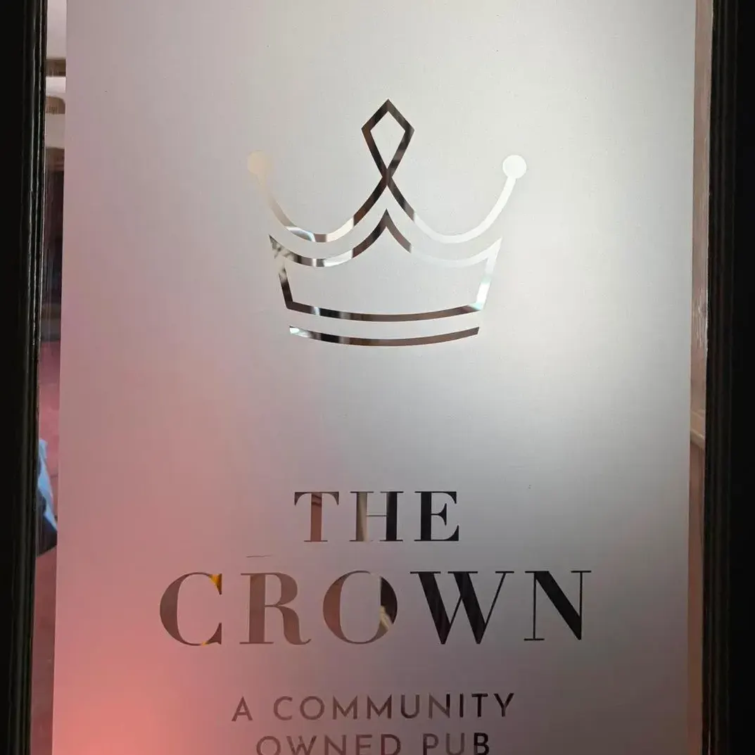An illuminated signage panel carrying a line-drawn crown above a name set in a fine serif