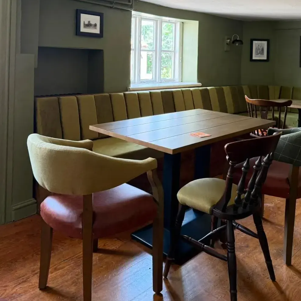 A panelled snug painted deep olive, with a long banquette, a wooden table and upholstered chairs