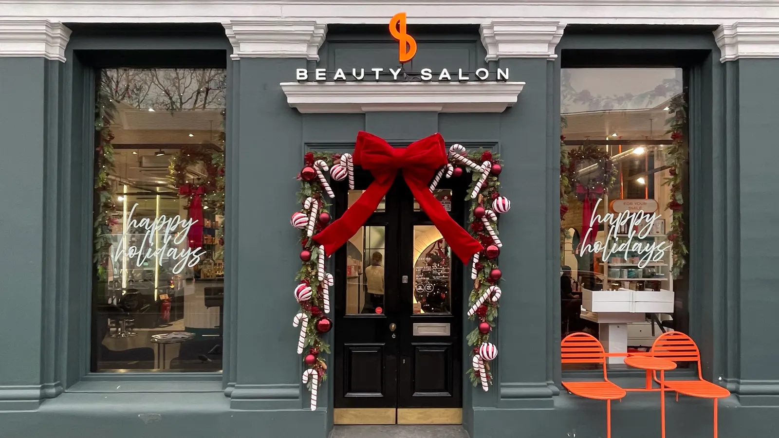 A dark teal shop frontage dressed for Christmas, a large red velvet bow and candy cane garlands framing the door