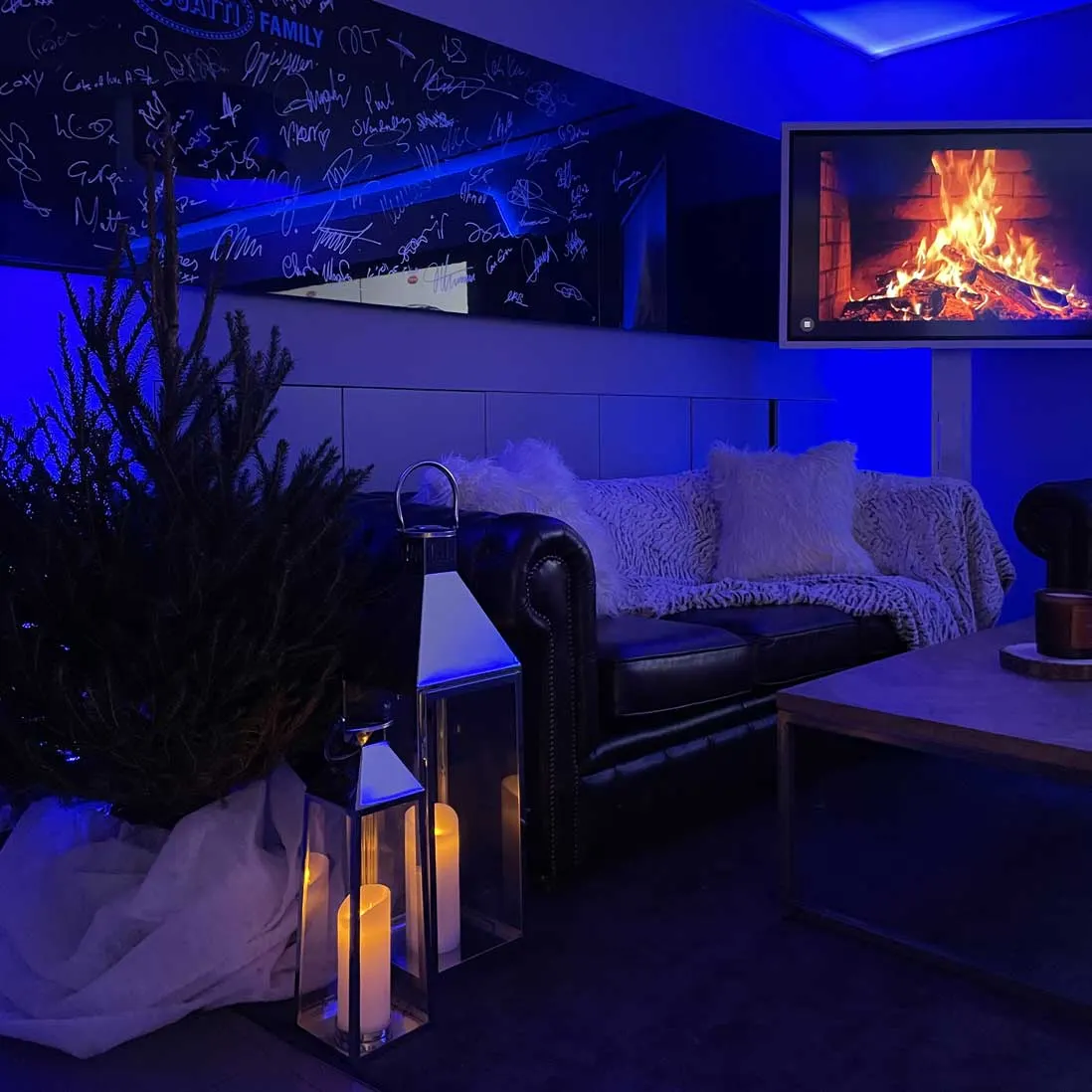 A dark sofa and lanterns lit blue beside a fire screen and artificial snow