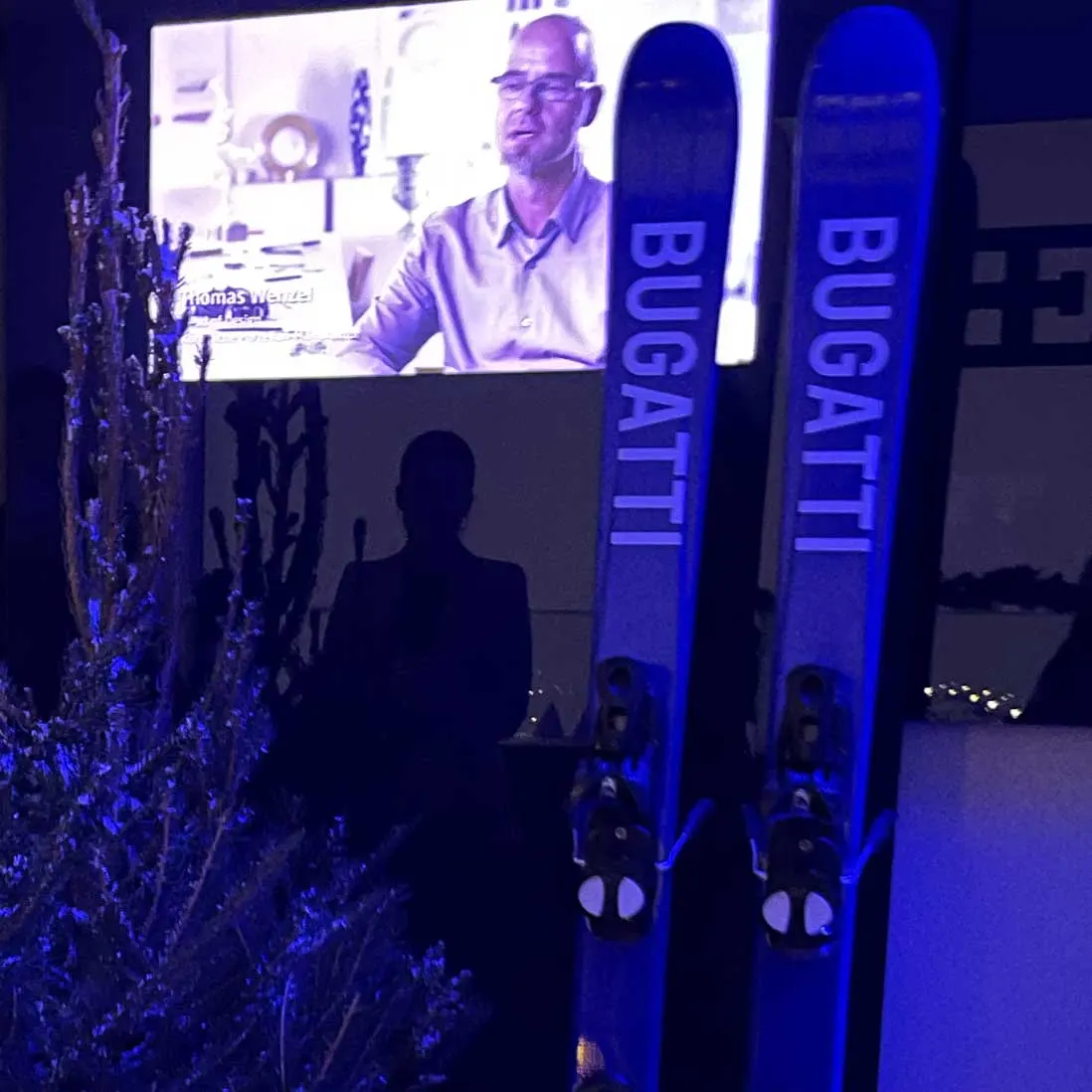 A pair of branded skis standing upright against a lit backdrop beside a presentation screen