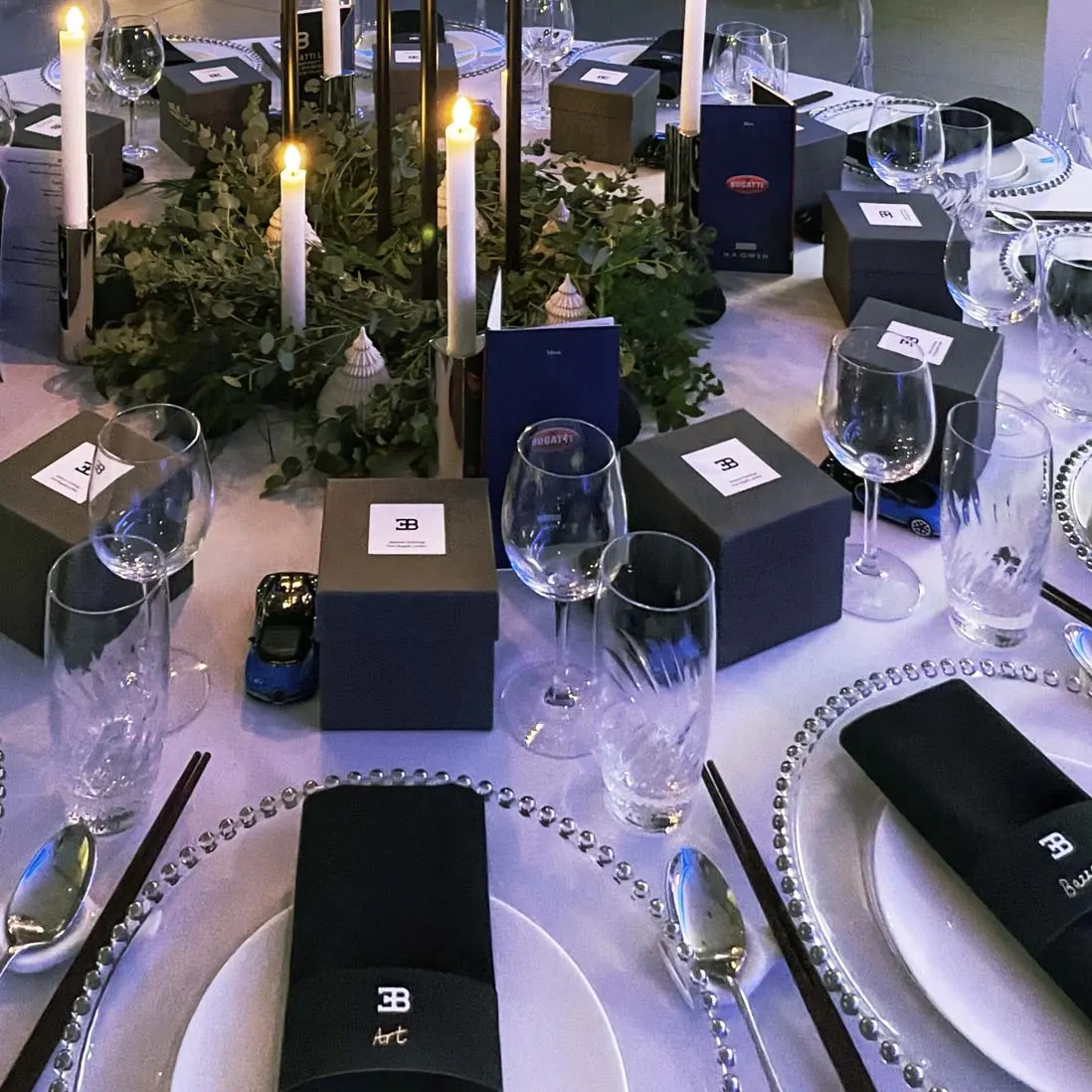 Place settings with wrapped gift boxes, foliage and lit candles down a dressed table