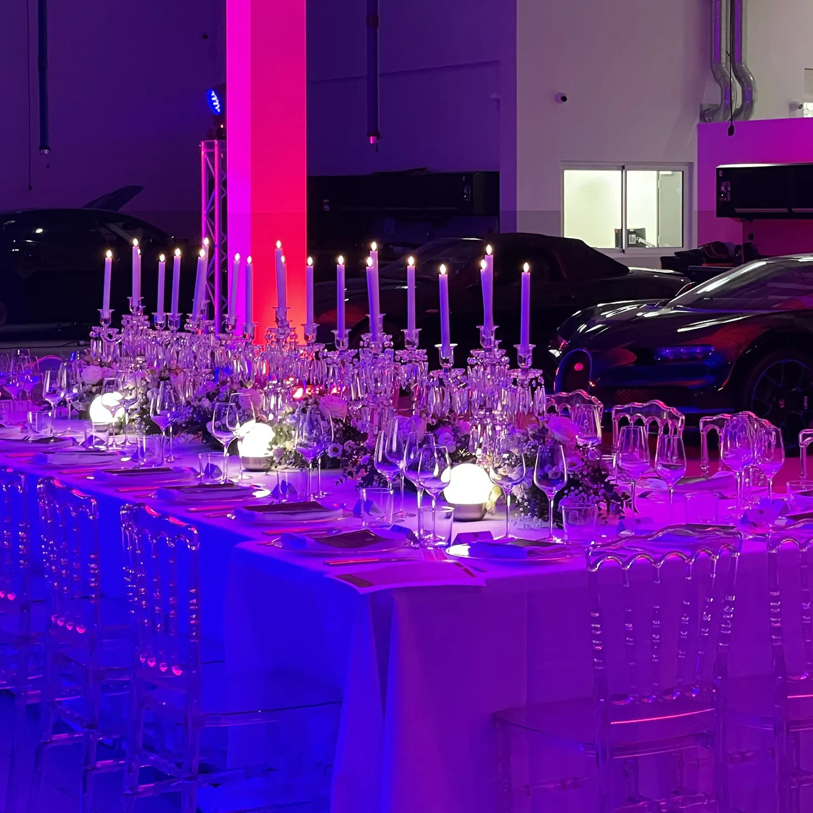 Candelabra and glassware along the dressed dinner table, with cars behind