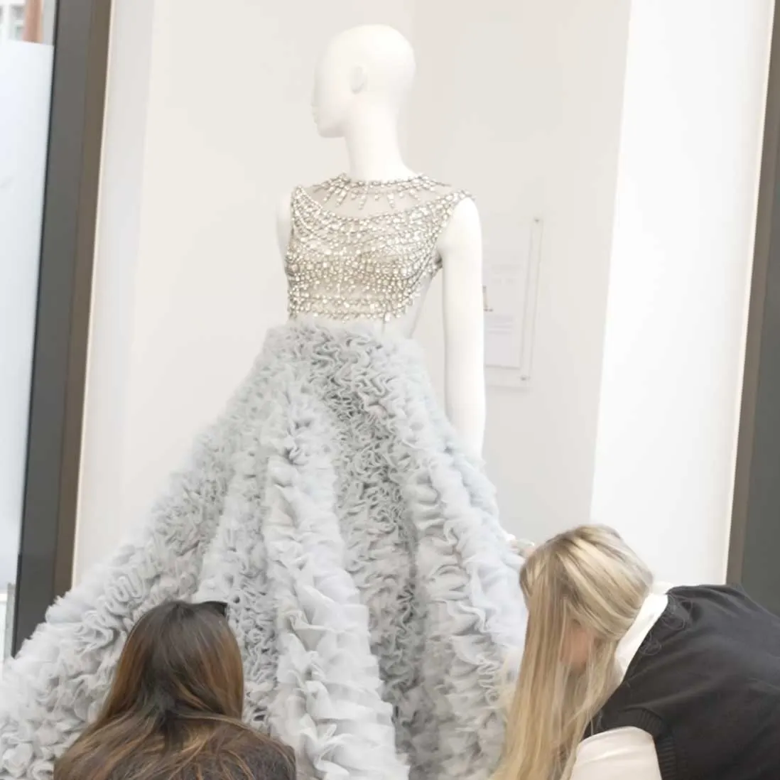 A beaded floor-length gown displayed on a mannequin behind two visitors