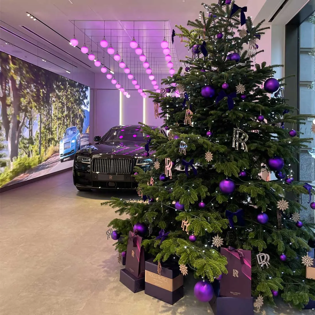 A tall Christmas tree dressed in purple and rose gold beside a car in a lit showroom