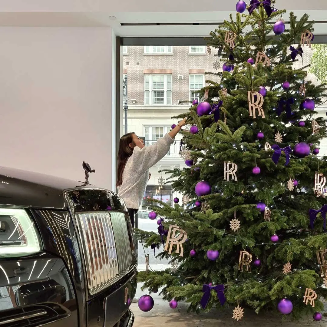 A stylist decorating a tall Christmas tree in a showroom window