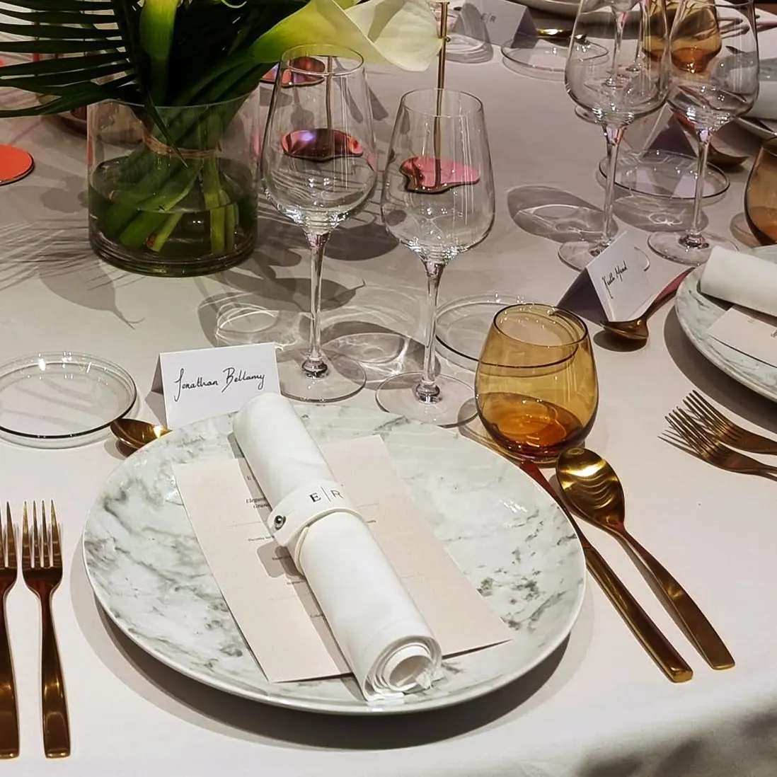 A place setting with a marble charger, gold cutlery, amber glass and a name card