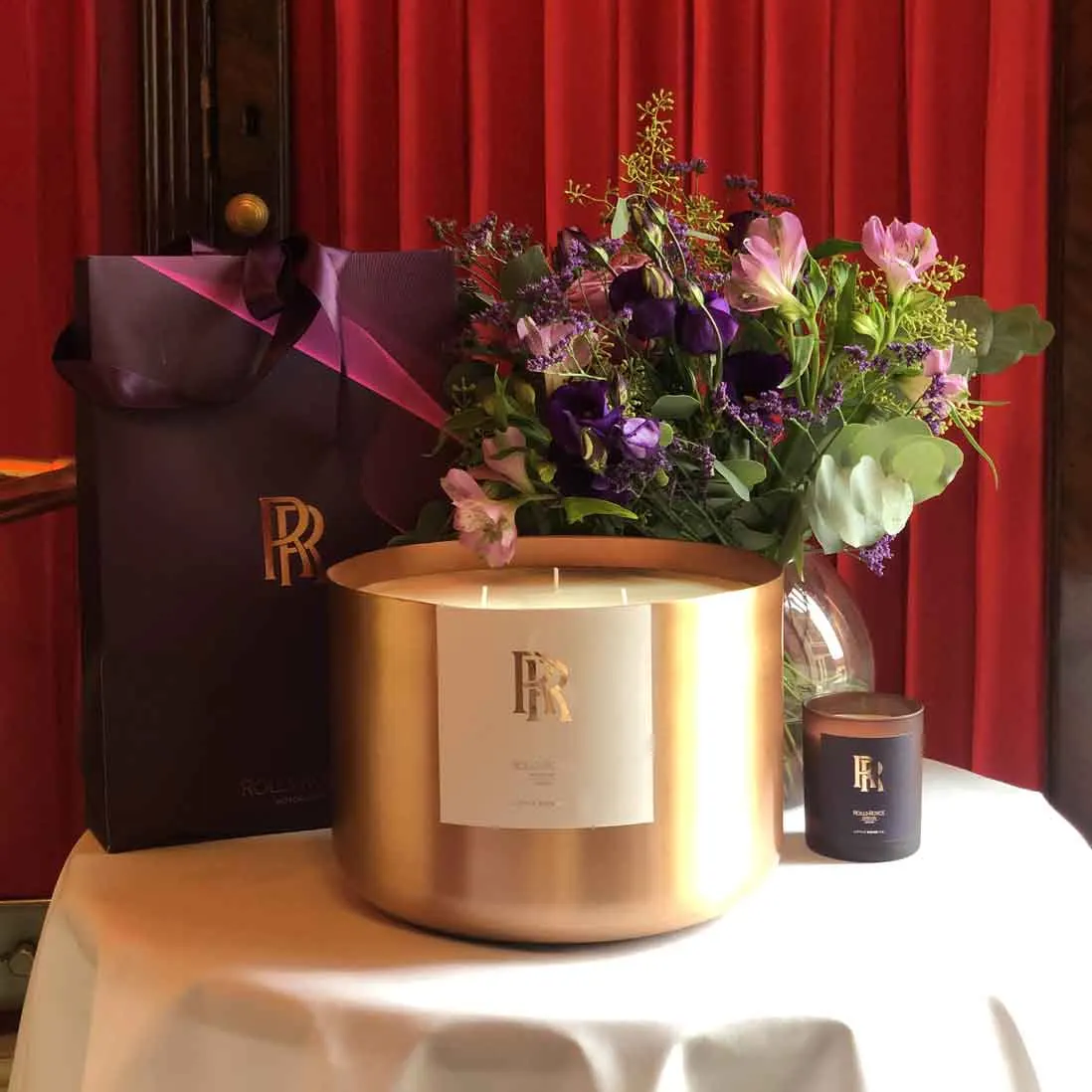 A large copper scented candle and a spring floral arrangement on a linen-covered table