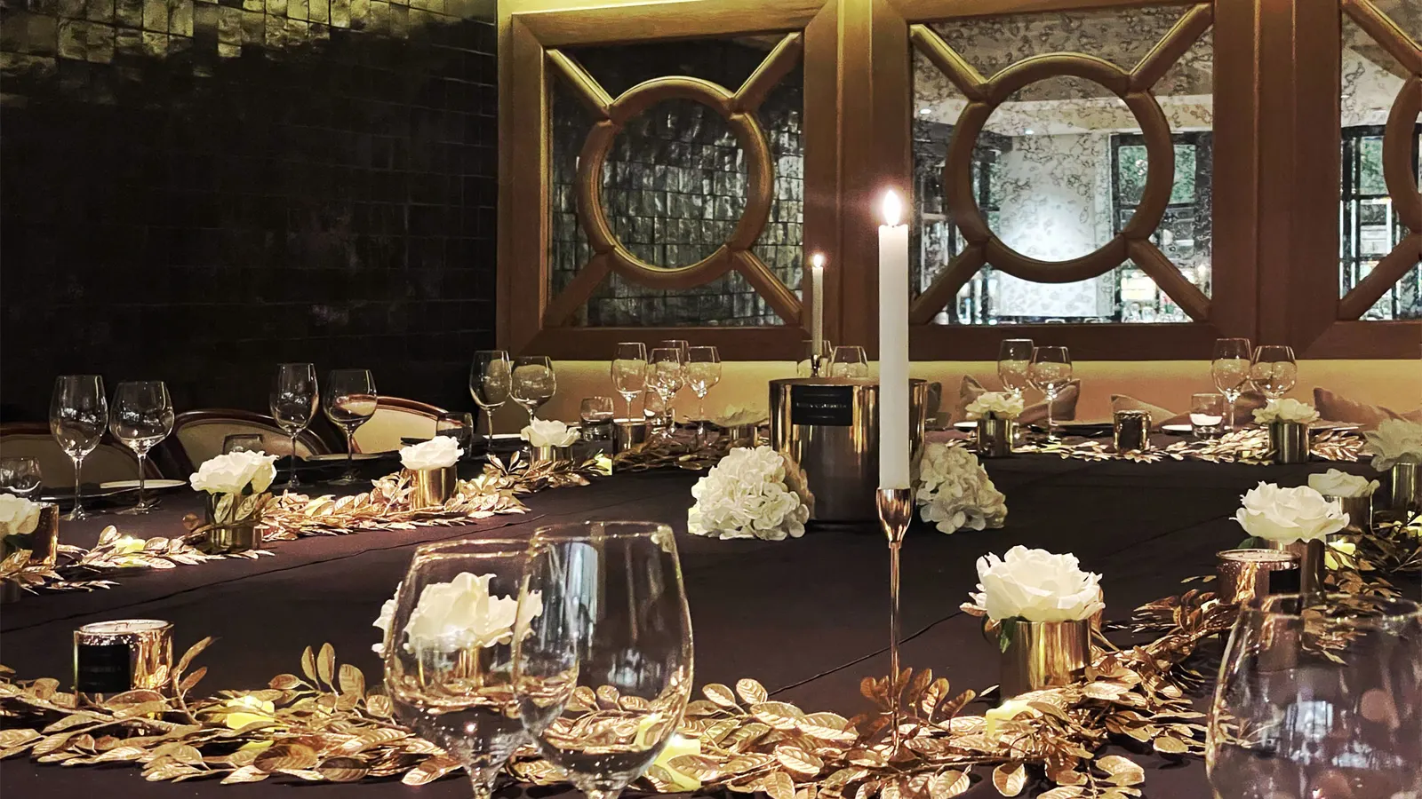 A candlelit dinner table dressed with gold foliage and white roses
