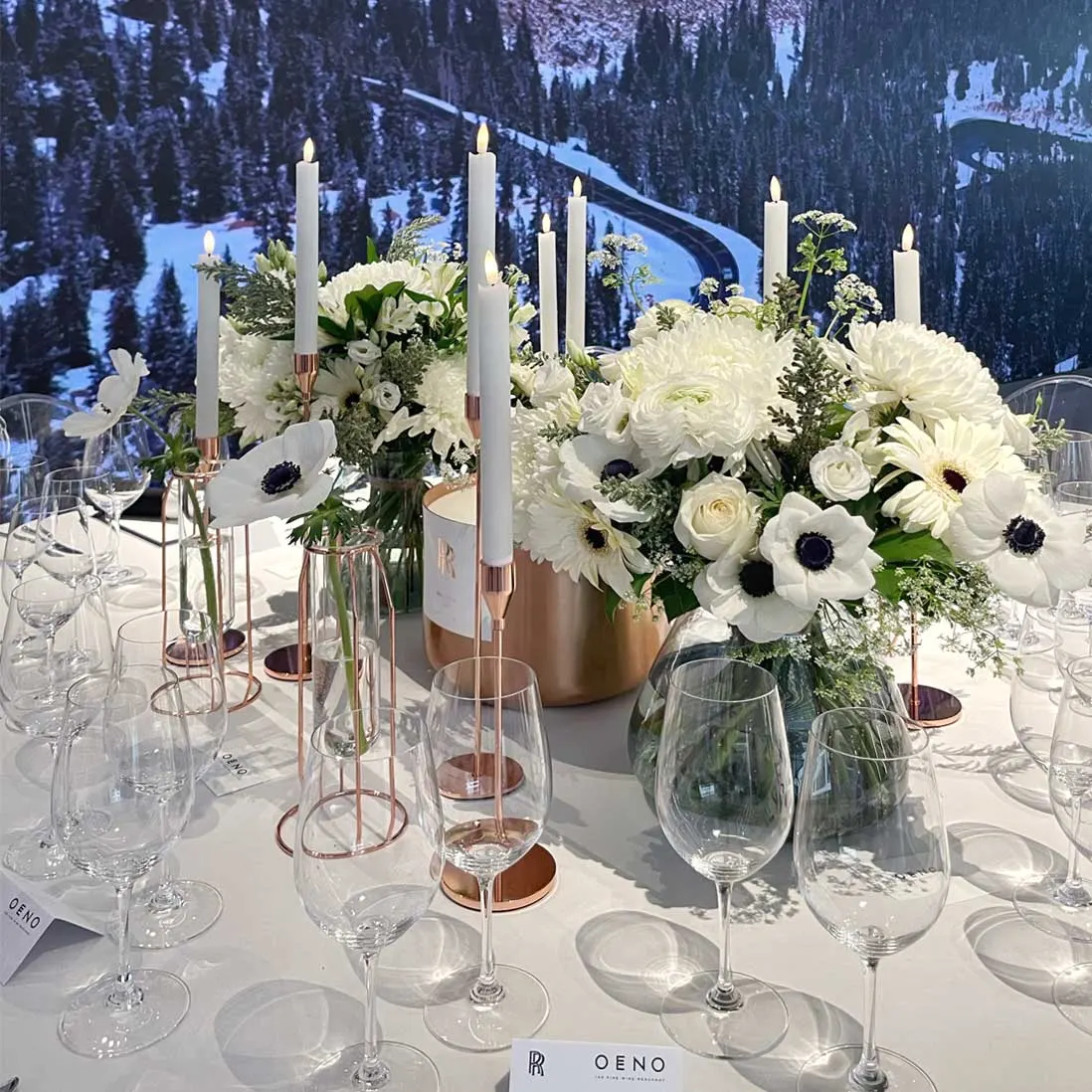 White anemones and tapered candles on a laid table in front of a lit screen