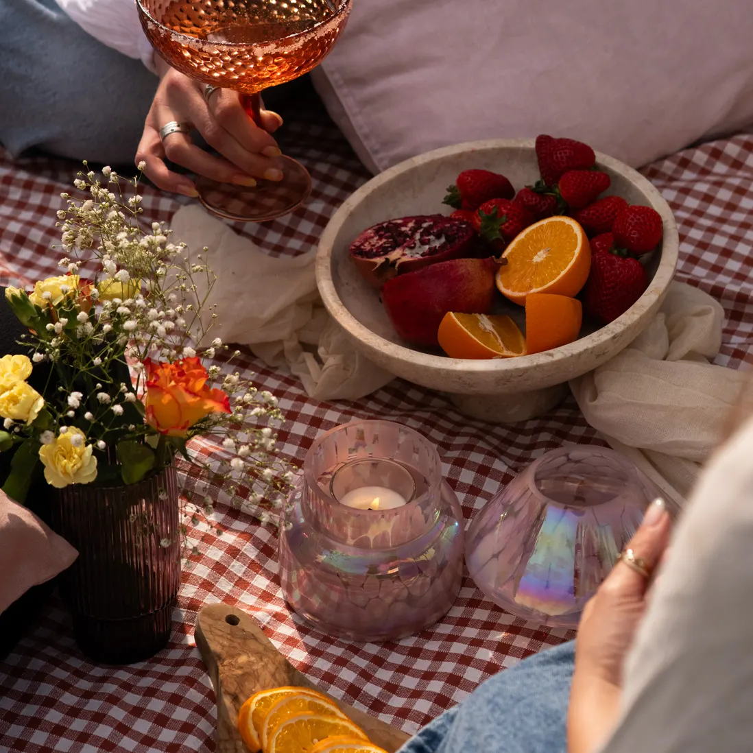 A bowl of pomegranate, orange and strawberries beside a lit candle and a small vase of roses