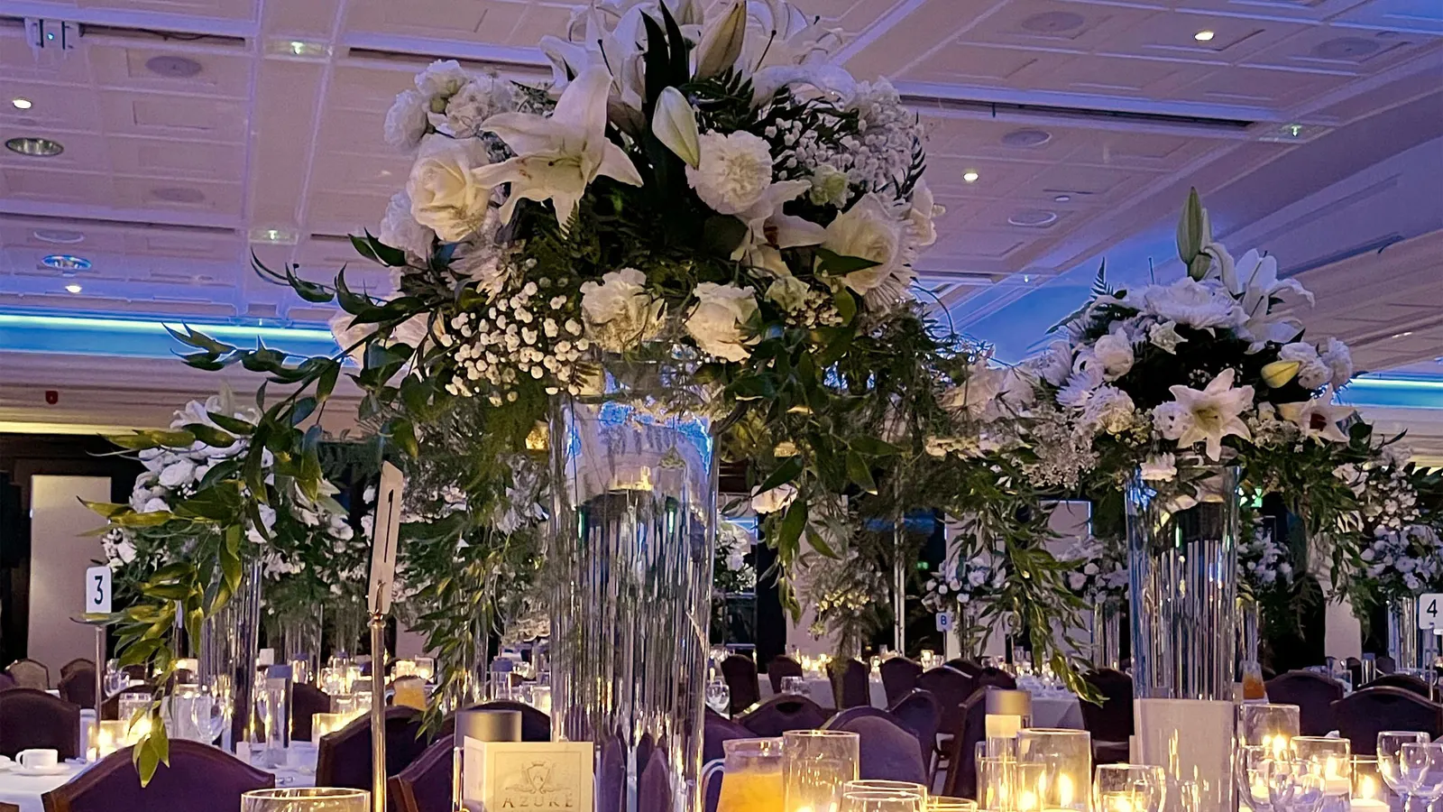Tall white floral centrepieces above a candlelit wedding breakfast