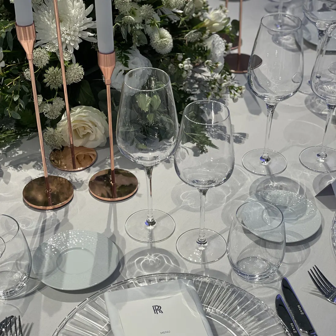 Copper candlesticks, glassware and white roses down a dressed table