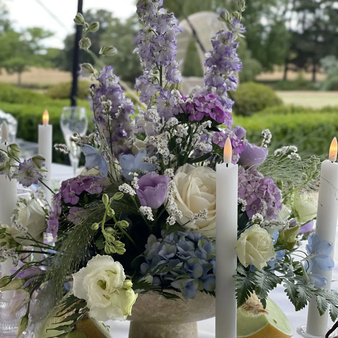 A centrepiece of delphiniums, hydrangea and roses between taper candles