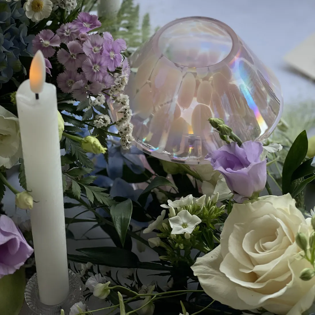 An iridescent glass shade set among florals and a lit candle