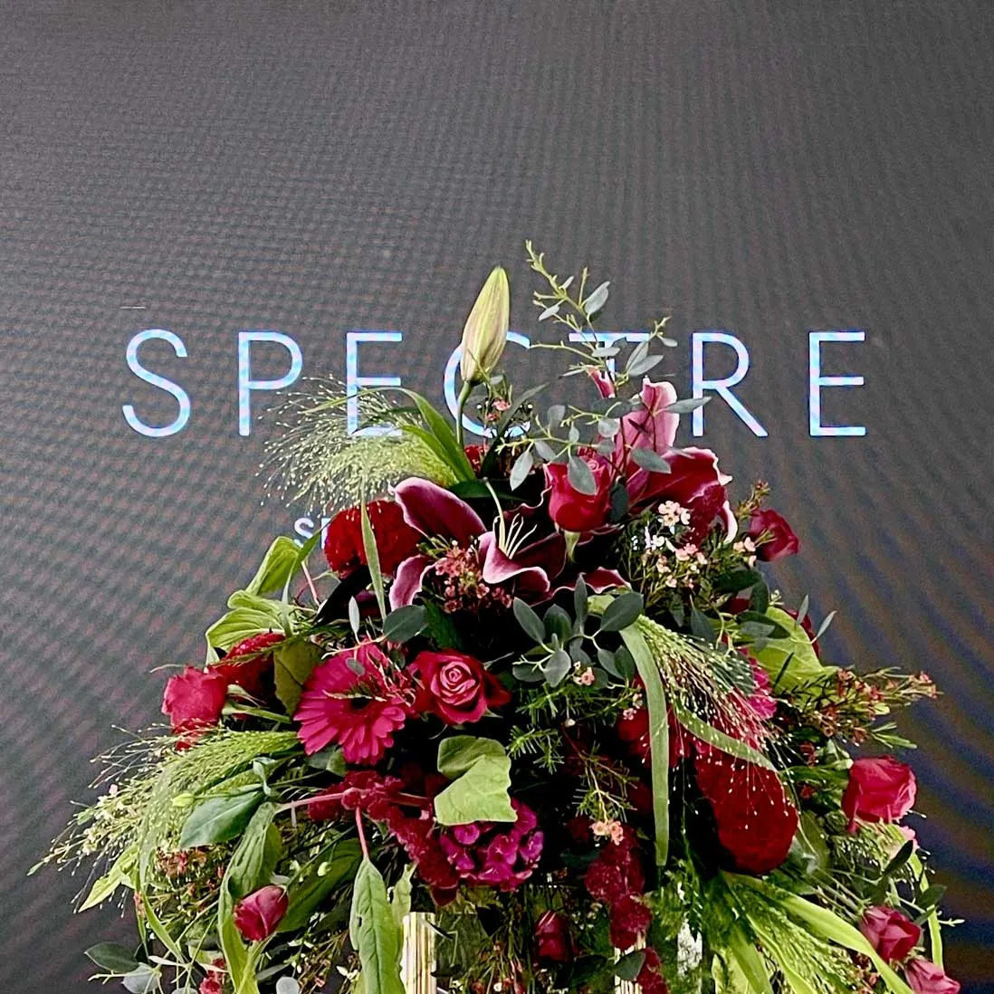 A large arrangement of red and burgundy blooms against a lit wall