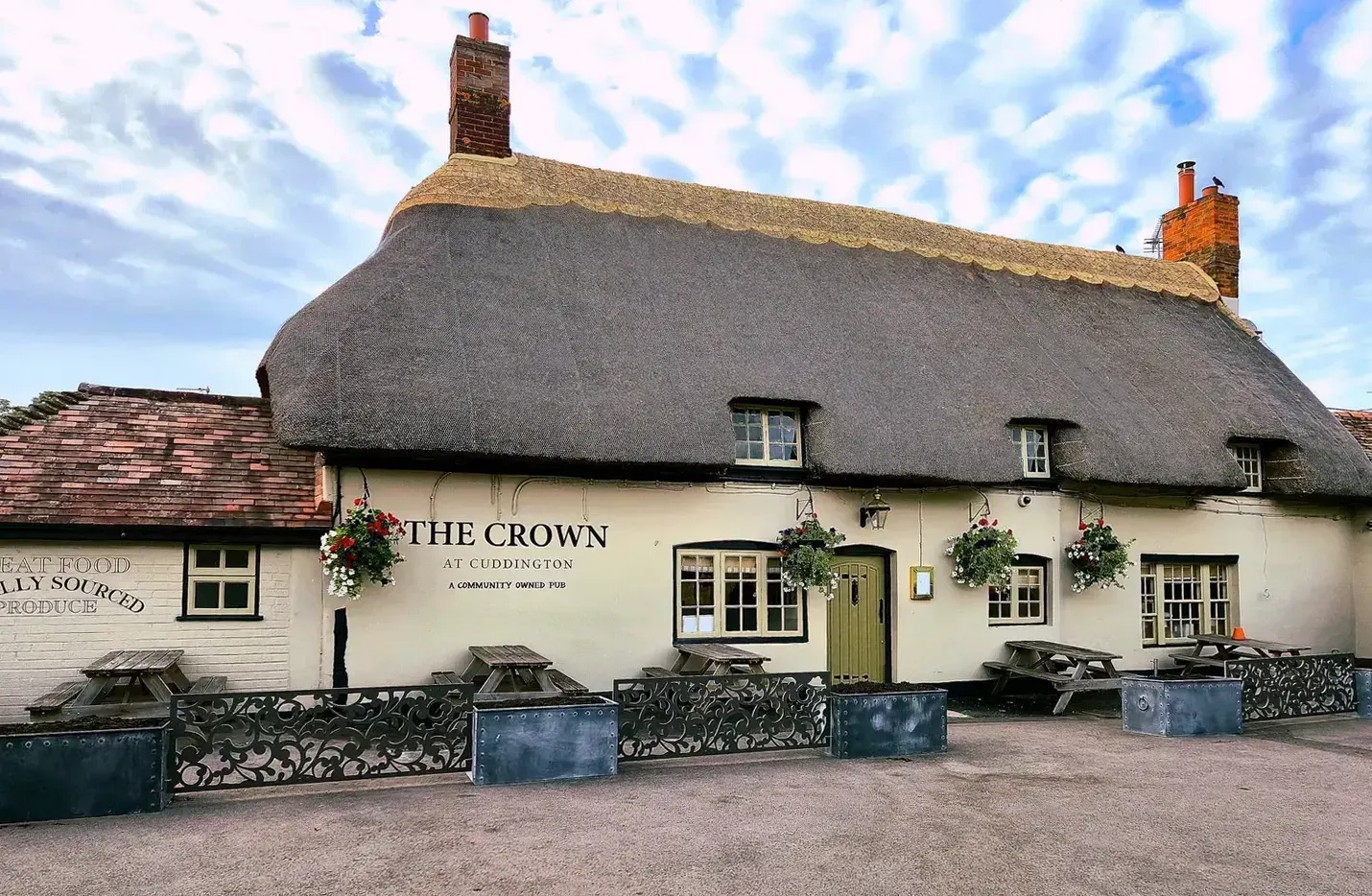 A thatched village pub with hanging baskets, benches and painted railings along its front