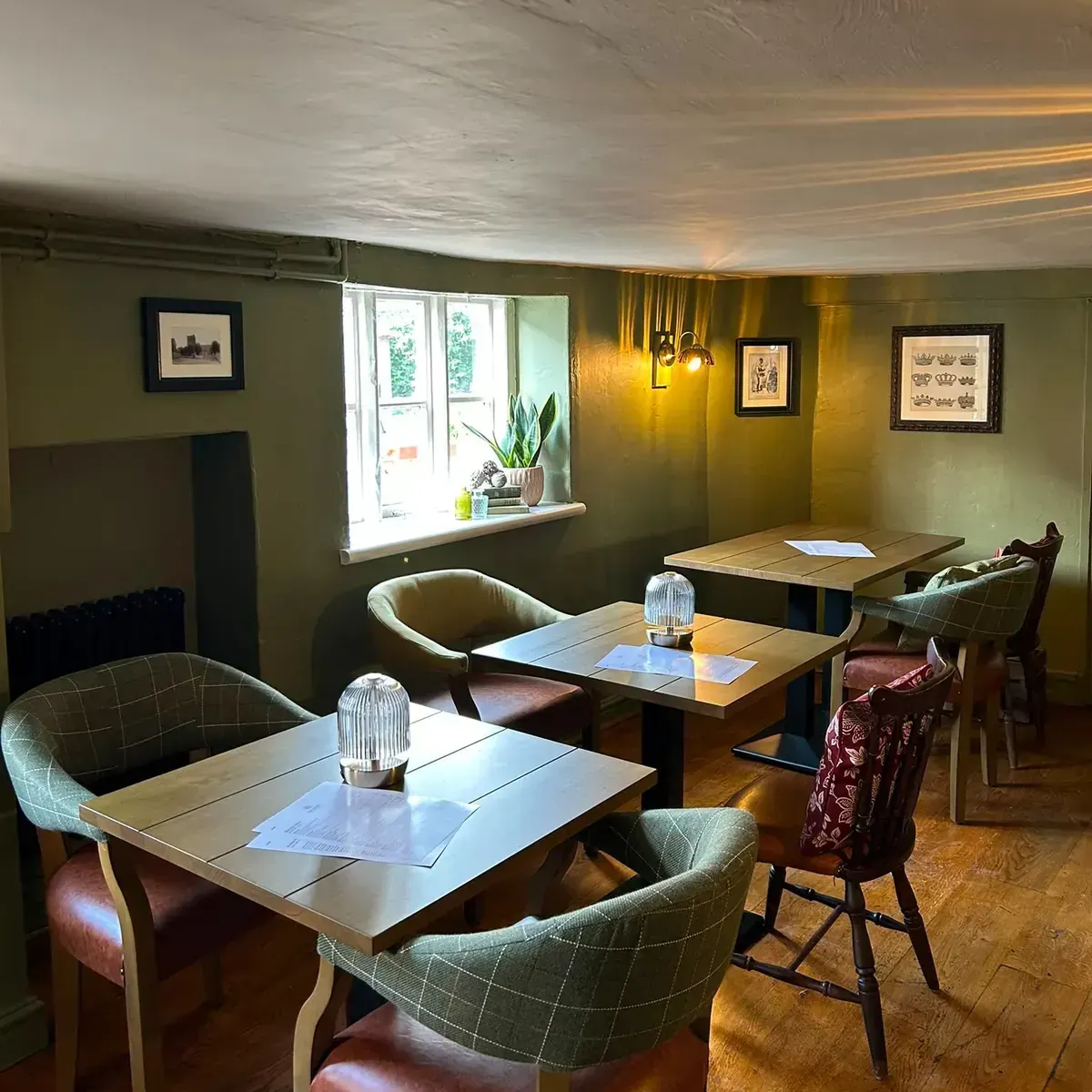 A dining room painted deep olive green, with framed prints and laid tables under a low ceiling