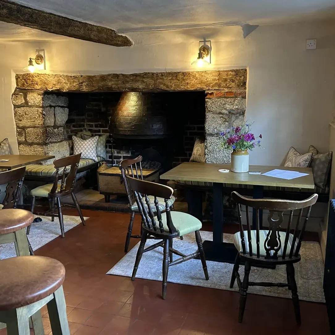 A stone inglenook fireplace with small tables and a jug of wildflowers in front of it